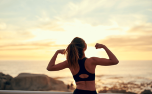 An image of a woman flexing muscles by the ocean, embodying habits for sustained wellness.